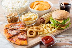 Ein Holztisch mit ungesundem Essen wie z.B. Burger, Chips und Pommes. 