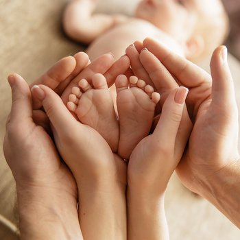 Zwei Händepaare der Eltern umranden die kleinen Füsse des Neugeborenen. 