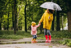 Eine Mutter mit Kind in Regenkleidung läuft glücklich durch den Regen.