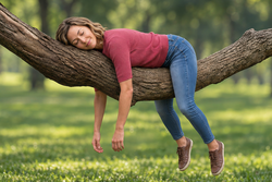 Eine Frau liegt mit herabhängenden müden Armen auf einem Baum. 