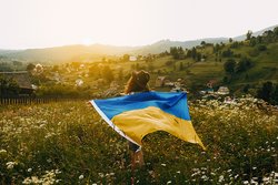 Eine Frau läuft mit einer Ukraine-Fahne über eine Blumenwiese. 